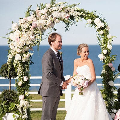 Bride and Groom standing in front of beautiful flowers at an outdoor wedding.