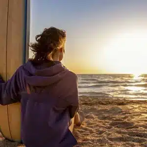 Surfer on beach with surfboard watching the sunset